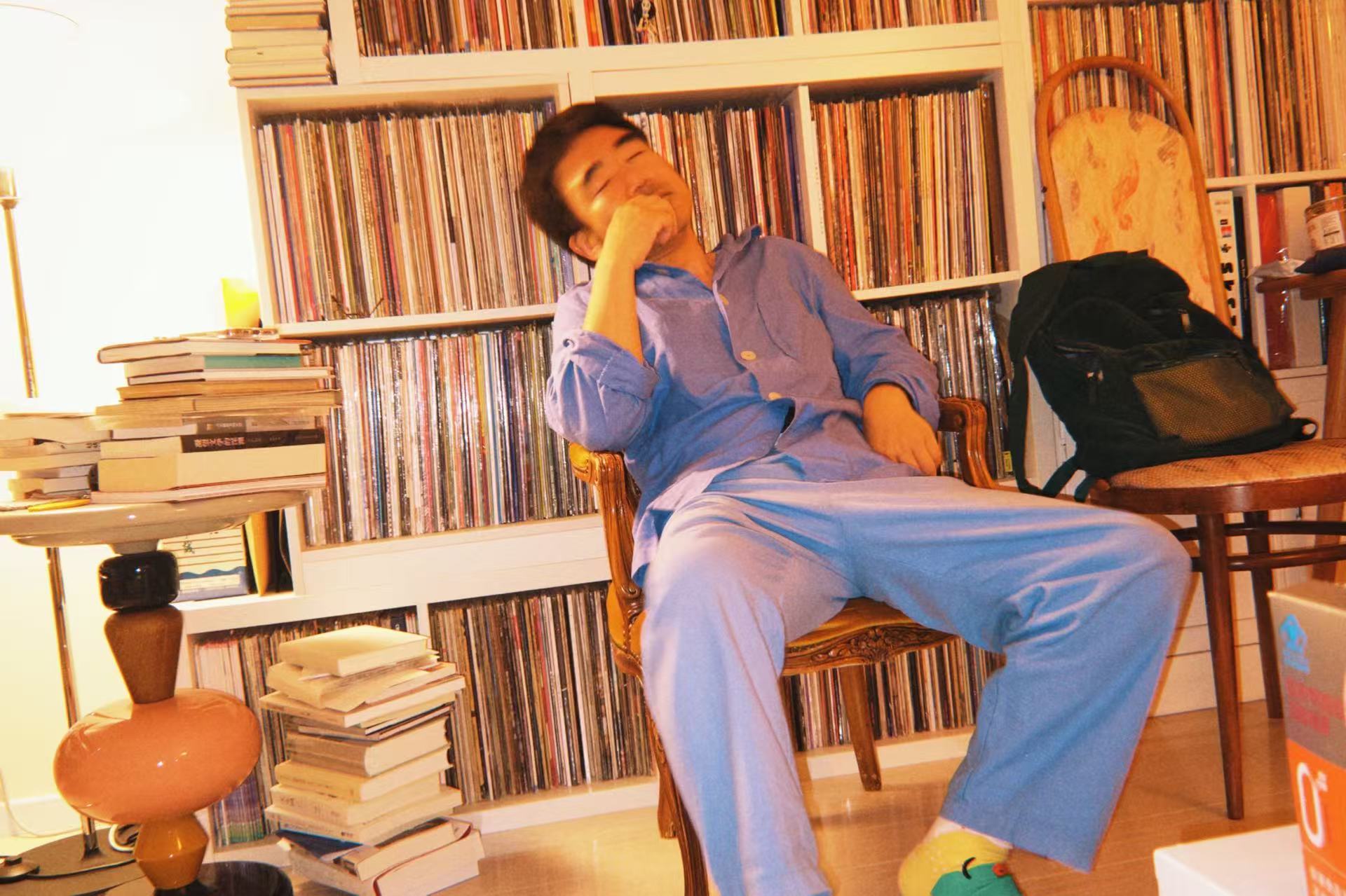 A photo of Meng on a chair, eyes closed, in front of his record collection